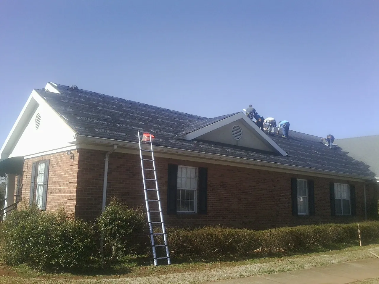 Crew tearing shingles off a brick ranch roof with a ladder set — Emergency Roof Repair work by our crew in Good Hope