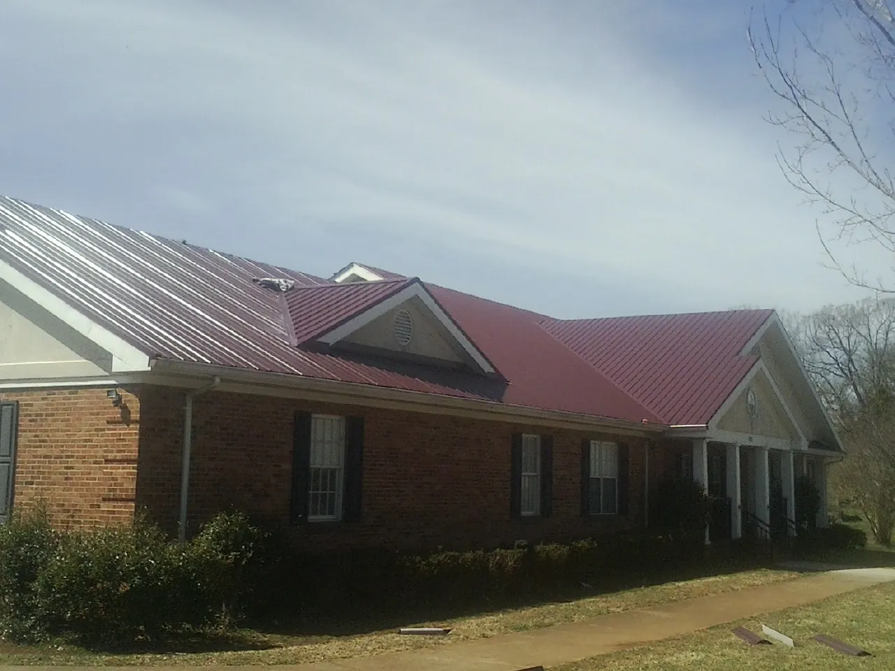 Red metal roof with gabled entries on a long brick building, from a Hail Damage Roof Repair job in Good Hope