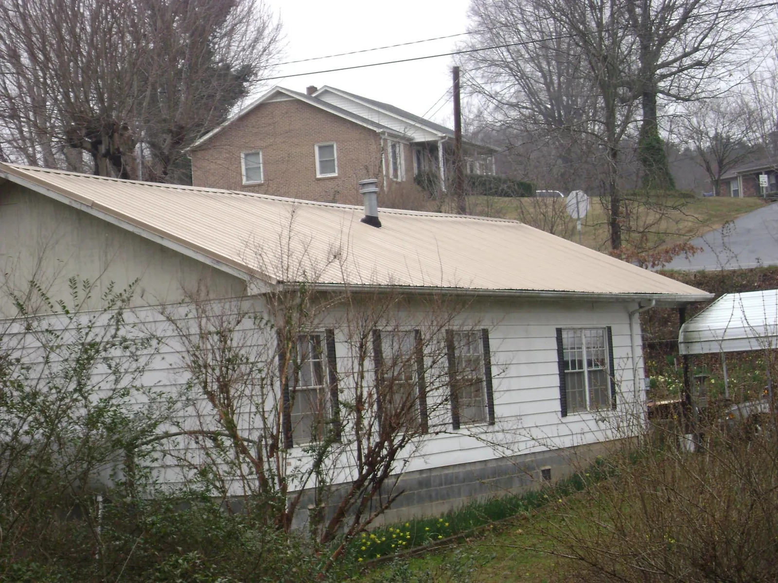 Tan metal roof on a white sided house set into a hillside — Commercial Roofing by Roofing Brothers in Good Hope